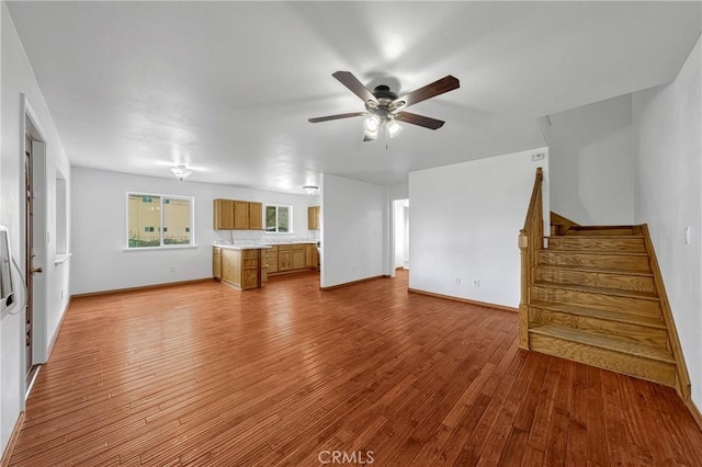 unfurnished living room featuring a ceiling fan, stairway, baseboards, and hardwood / wood-style flooring