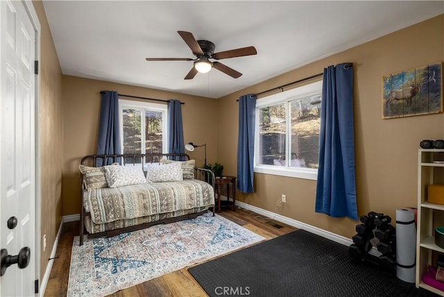 bedroom with a ceiling fan, wood finished floors, visible vents, and baseboards