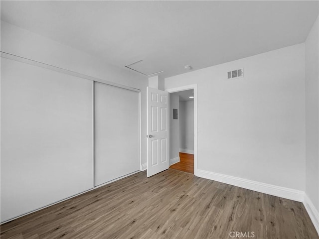 unfurnished bedroom featuring baseboards, a closet, visible vents, and wood finished floors