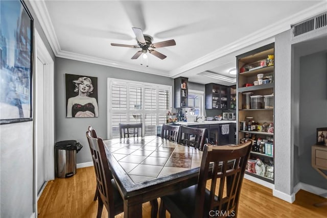 dining room with a ceiling fan, crown molding, light wood-style flooring, and baseboards