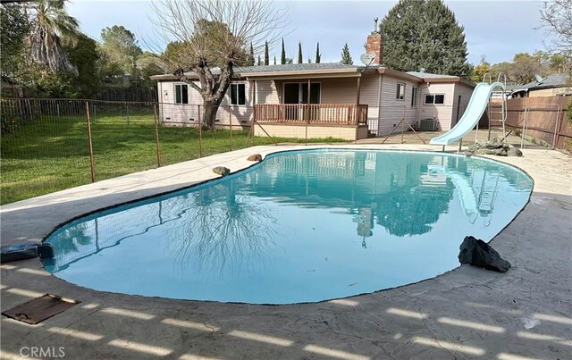 view of swimming pool with a wooden deck, a water slide, a fenced in pool, a fenced backyard, and a yard