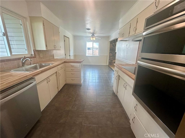 kitchen featuring tasteful backsplash, dark tile patterned flooring, appliances with stainless steel finishes, a peninsula, and a sink