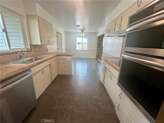 kitchen featuring stainless steel appliances, dark tile patterned flooring, decorative backsplash, a sink, and a ceiling fan