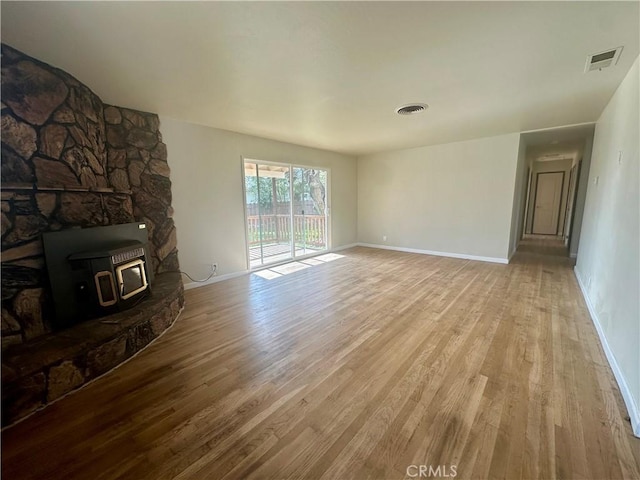 unfurnished living room with light wood-style flooring, baseboards, a wood stove, and visible vents