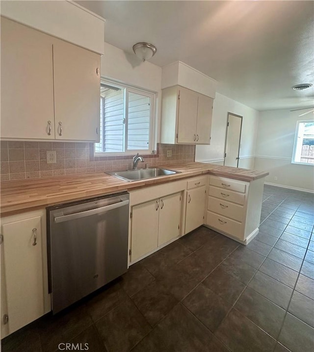 kitchen with a peninsula, butcher block countertops, a sink, stainless steel dishwasher, and backsplash