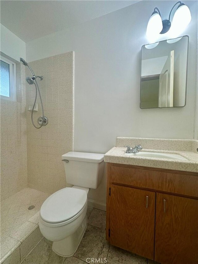 full bath featuring toilet, vanity, baseboards, and a tile shower