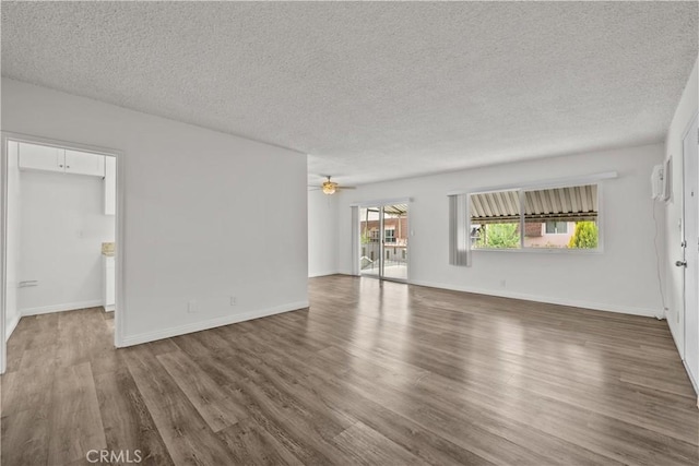 unfurnished living room with a textured ceiling, wood finished floors, a ceiling fan, baseboards, and a wall mounted AC