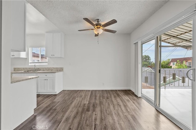 kitchen with a textured ceiling, baseboards, white cabinets, and wood finished floors