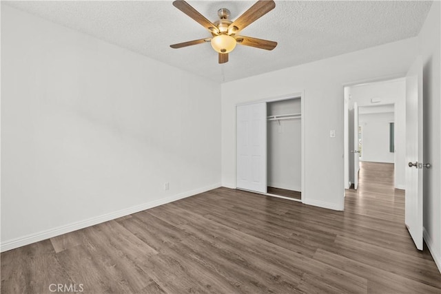 unfurnished bedroom featuring a closet, dark wood-style flooring, a textured ceiling, and baseboards