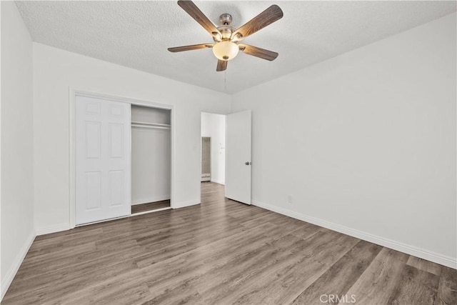 unfurnished bedroom with a closet, a textured ceiling, baseboards, and wood finished floors