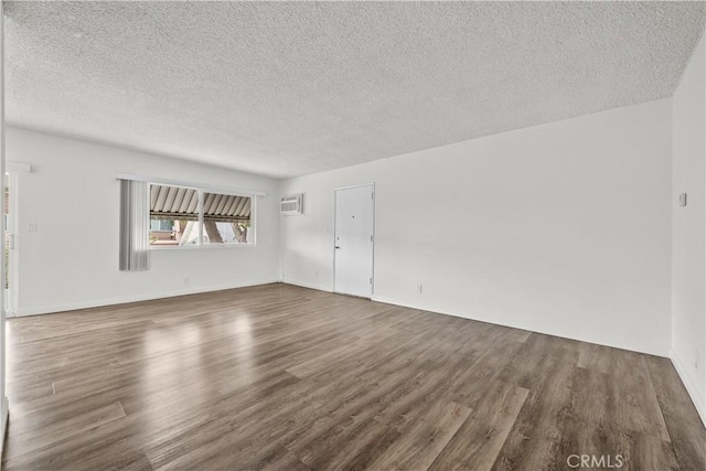 empty room featuring a textured ceiling, dark wood-style flooring, and a wall mounted air conditioner