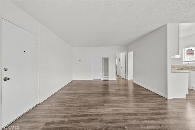 unfurnished living room featuring a sink, a textured ceiling, and wood finished floors