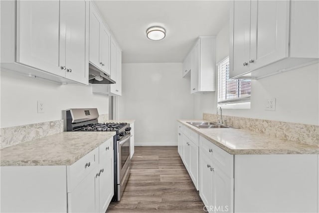 kitchen with under cabinet range hood, a sink, wood finished floors, light countertops, and stainless steel range with gas cooktop