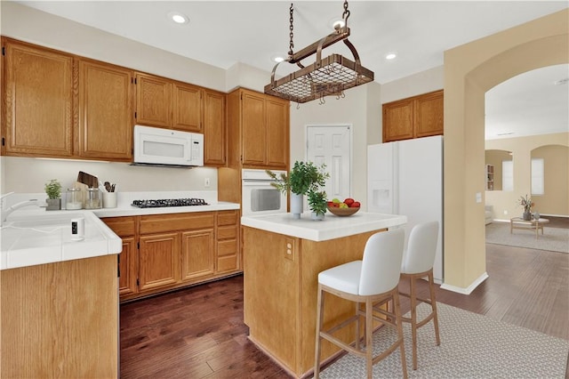 kitchen featuring white appliances, arched walkways, a kitchen island, dark wood-type flooring, and a sink