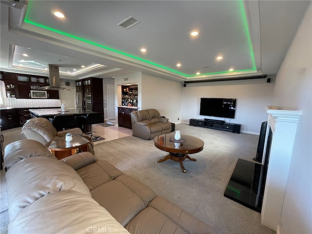 carpeted living area featuring baseboards, a raised ceiling, visible vents, and recessed lighting