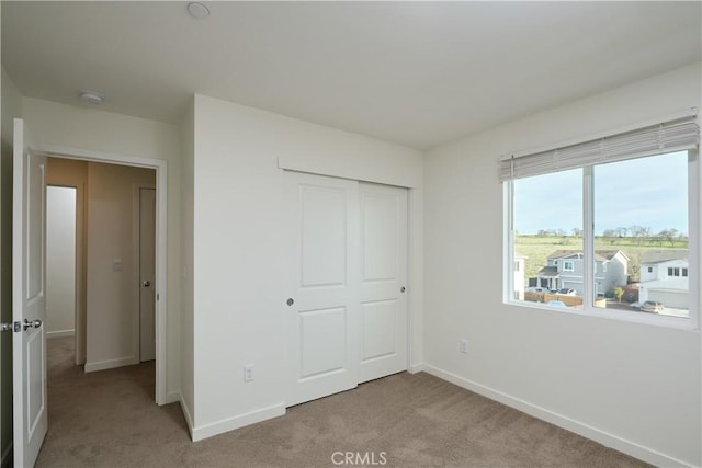 unfurnished bedroom with a closet, light colored carpet, and baseboards