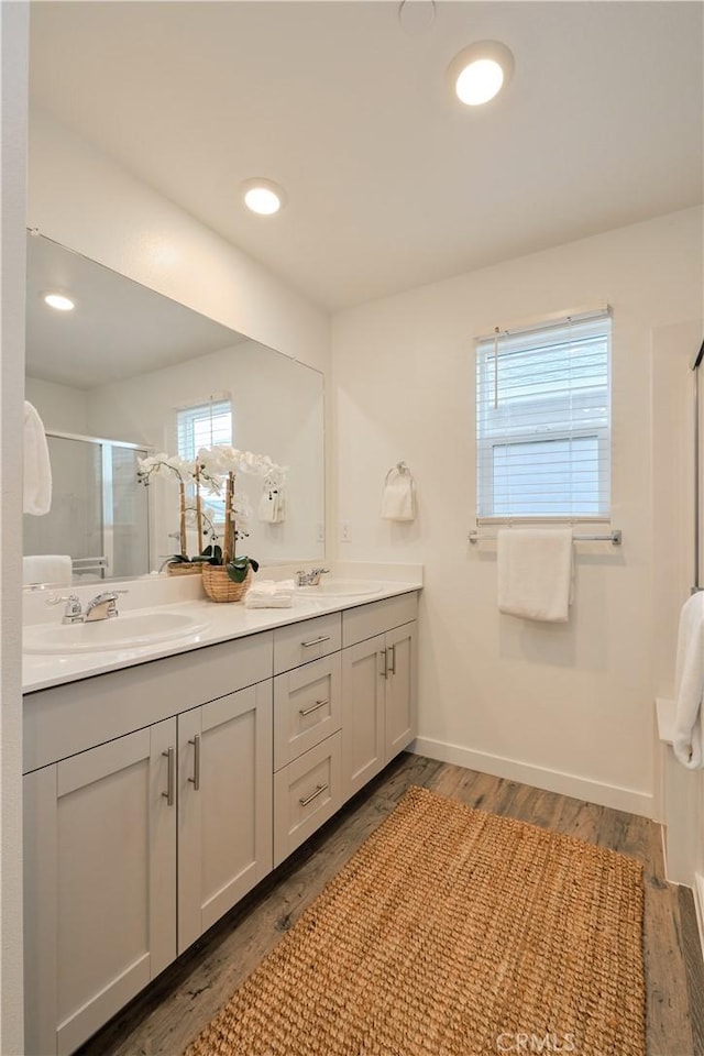 full bathroom with double vanity, baseboards, wood finished floors, a shower stall, and a sink