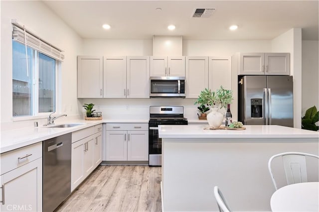 kitchen with stainless steel appliances, light countertops, visible vents, light wood-style flooring, and a sink