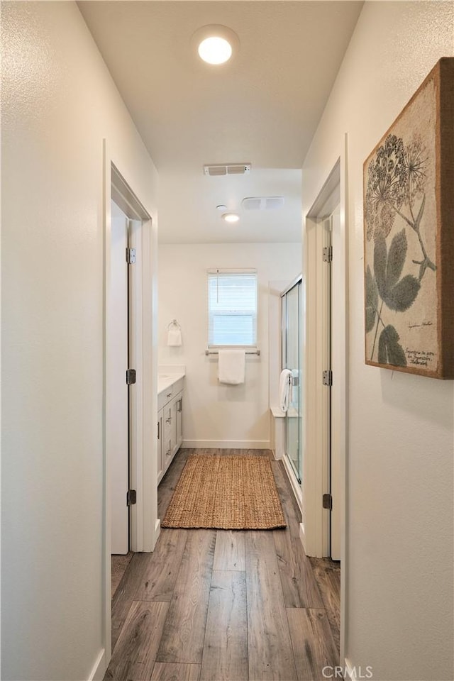 hall with baseboards, visible vents, and wood finished floors