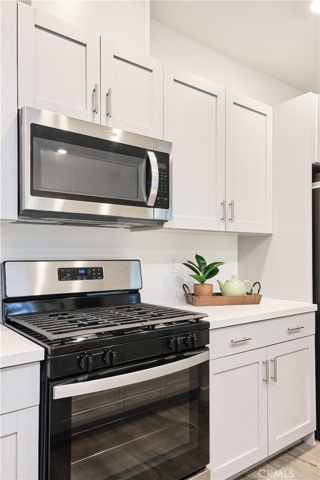 kitchen featuring light wood-type flooring, white cabinets, stainless steel appliances, and light countertops