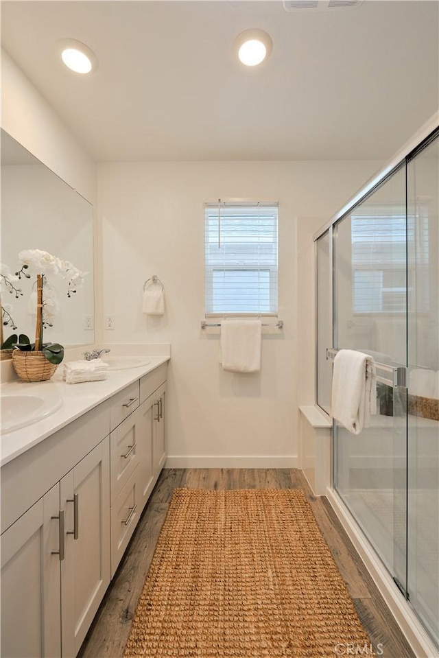 full bath featuring double vanity, a sink, a shower stall, and wood finished floors