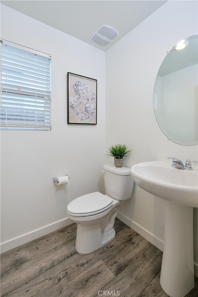 bathroom with baseboards, visible vents, toilet, and wood finished floors