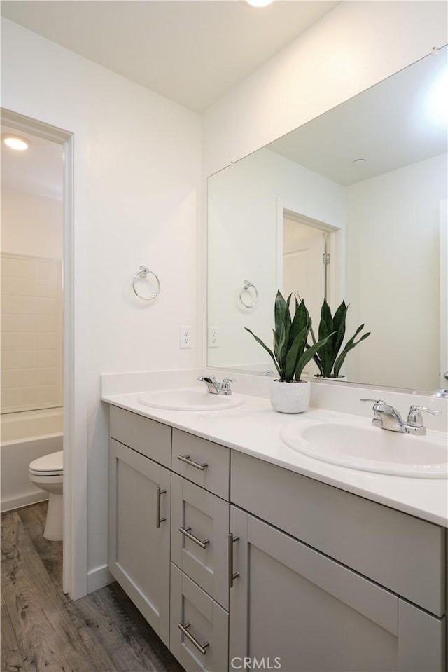 bathroom with double vanity, toilet, a sink, and wood finished floors