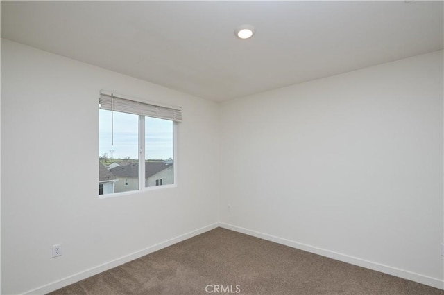 empty room featuring dark colored carpet and baseboards