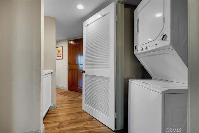 laundry room featuring baseboards, laundry area, stacked washer / dryer, and light wood-style floors