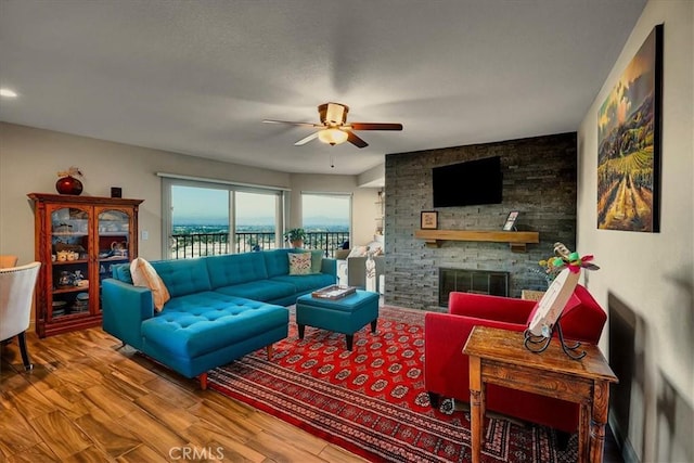 living area with ceiling fan, a stone fireplace, and wood finished floors