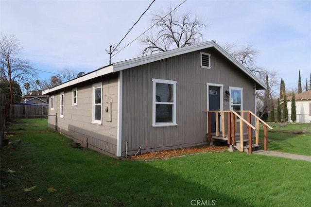 rear view of property featuring a lawn and fence