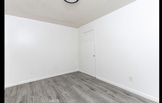 empty room featuring a textured ceiling, baseboards, and wood finished floors