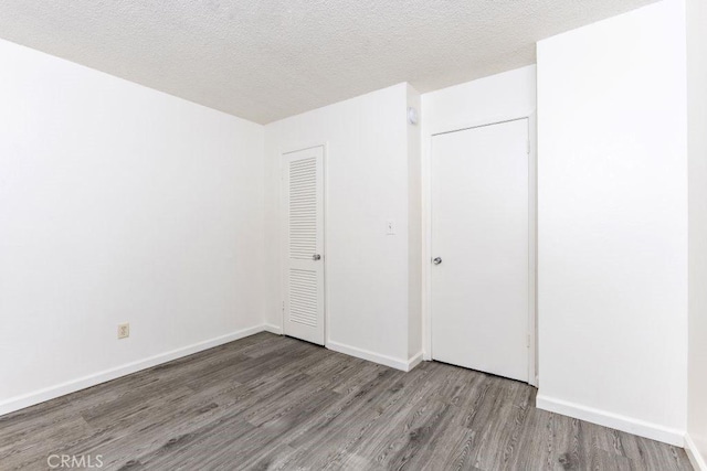 unfurnished bedroom featuring a closet, a textured ceiling, baseboards, and wood finished floors