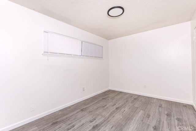 spare room featuring a textured ceiling, baseboards, and wood finished floors