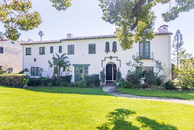 mediterranean / spanish home with a chimney, a front yard, a tile roof, and stucco siding