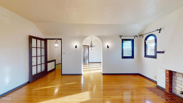 unfurnished room featuring arched walkways, a fireplace, vaulted ceiling, and light wood-style flooring