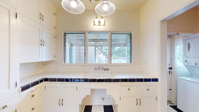 kitchen featuring stacked washer and dryer, backsplash, a sink, and white cabinets