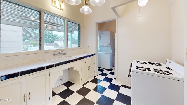 kitchen with tile counters, stacked washer / drying machine, white gas range, light floors, and a sink