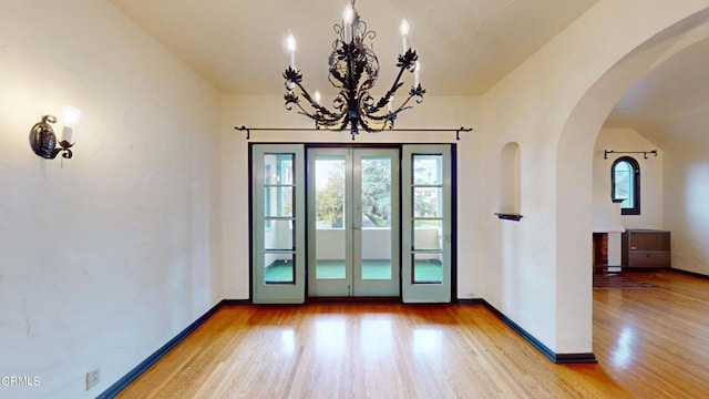 interior space with baseboards, arched walkways, wood finished floors, french doors, and a chandelier