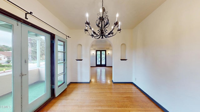 interior space featuring arched walkways, a notable chandelier, baseboards, french doors, and light wood finished floors