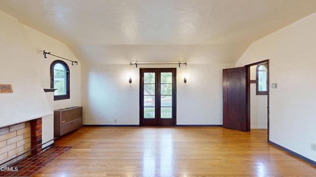 unfurnished living room with light wood-style floors, lofted ceiling, french doors, and plenty of natural light