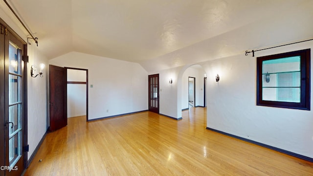 spare room featuring vaulted ceiling, arched walkways, light wood-style flooring, and baseboards