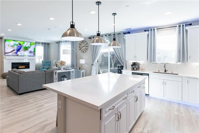 kitchen featuring tasteful backsplash, dishwasher, light wood-style flooring, light countertops, and a sink