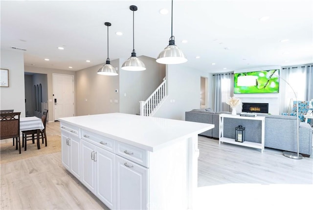 kitchen with light wood-style flooring, recessed lighting, white cabinets, a center island, and a glass covered fireplace