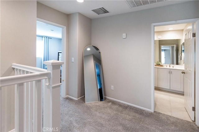 hall with an upstairs landing, baseboards, visible vents, and light colored carpet