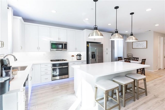 kitchen with light wood-style flooring, stainless steel appliances, a sink, white cabinetry, and backsplash