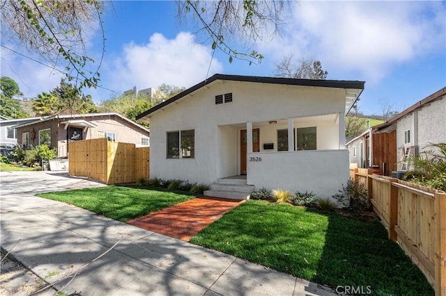 bungalow-style home featuring fence, a front lawn, and stucco siding