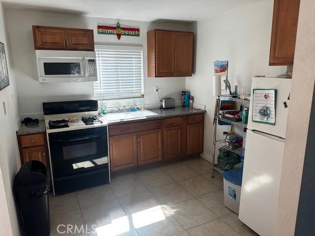 kitchen with brown cabinets, light tile patterned flooring, a sink, and white appliances