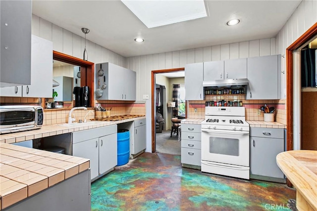 kitchen with tile countertops, concrete flooring, a sink, white range with gas cooktop, and decorative backsplash