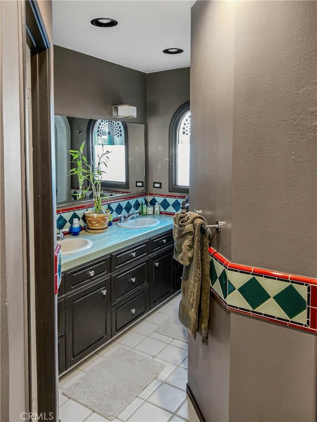 full bath with double vanity, tile patterned flooring, a sink, and a textured wall